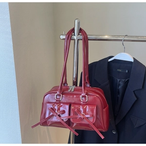 Close-up of deep red glossy patent leather bag featuring silver hardware and bow details