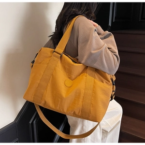 Detail of a large yellow travel tote bag featuring a round logo and crossbody strap