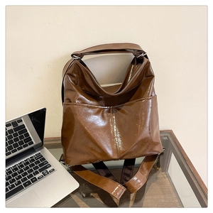 Dettaglio della borsa tote in pelle cerata marrone lucida con tasche frontali su scrivania
