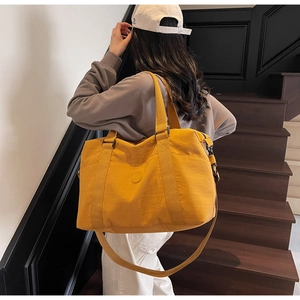 Detailed view of yellow travel tote bag with circular logo and detachable shoulder strap