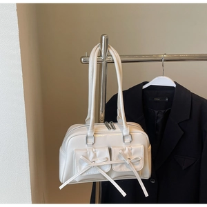Detail of cream patent leather bowling bag with bow-decorated pockets and silver hardware
