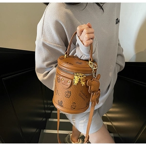 Detail view of the brown leather texture and Keddy Bear University prints on the bucket bag