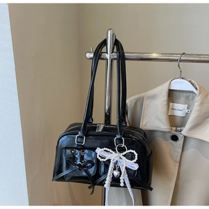 Detail of black glossy handbag with bow pockets and pearl lace heart pendant