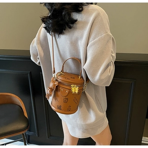Detailed view of brown cylinder bucket bag with teddy bear pattern and cute charm