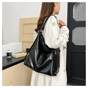 Dettaglio di una grande borsa tote nera lucida con tasca laterale indossata da una modella