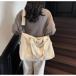 Close-up of large beige travel tote bag showing adjustable wide shoulder strap and handles