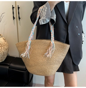 Dettaglio della borsa in paglia con manici intrecciati colorati e nappe decorative