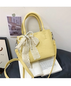 Dettaglio della borsa in pelle gialla con fiocco in pizzo bianco e decoro di perle