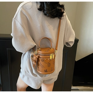 Detail of a brown leather cylinder bucket bag with bear print and plush charm on a model