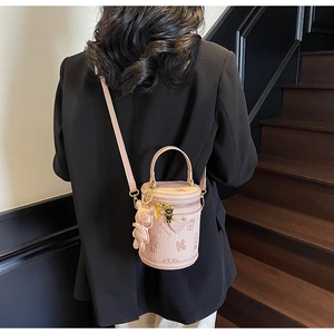 Pink cylindrical bucket bag with letter embossing and cute bear charm shown on model