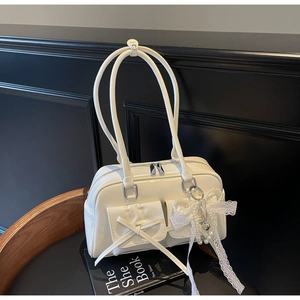 Detail of white glossy shoulder bag featuring double pockets with bow and pearl charms