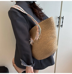 Dettaglio della borsa tote in paglia intrecciata con tracolla larga colorata e nappe