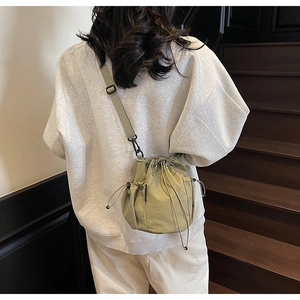 Model trägt eine kleine olivgrüne Umhängetasche mit Kordelzug und praktischer Netztasche