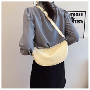 Detail of a creamy half-moon crossbody bag with litchi texture on a model's shoulder