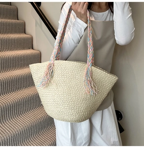 Dettaglio della borsa tote in paglia beige con manici intrecciati colorati e frange