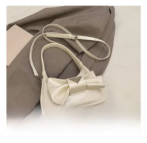 Detail of cream bow shoulder bag with silver triangle plaque on gray suit background