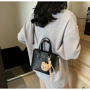 Detail of black woven tote bag featuring a cute plush bear charm and crossbody strap