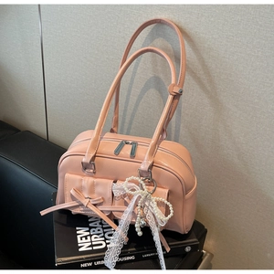 Close-up of pink glossy leather bag with bow detail and lace pearl charm accessory