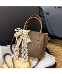 Dettaglio borsa a secchiello in pelle marrone con fiocco di pizzo e perle e goffratura