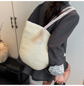 Dettaglio di una borsa tote in paglia beige con spalline colorate e decoro a frange