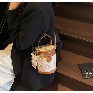 Detail of a beige cylinder bag with teddy bear print and brown leather trim on a model