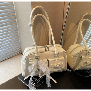 Close-up of cream white glossy leather shoulder bag with lace pearl bow charm detail