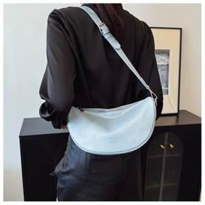 Close-up of a light blue crescent shoulder bag with pebbled leather and gold logo detail