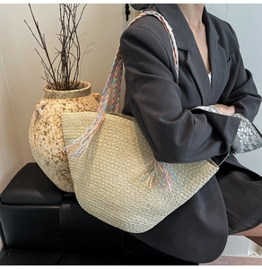 Dettaglio della borsa in paglia intrecciata con nappe colorate sulla tracolla intrecciata