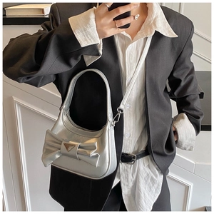 Detail of silver bow handbag with triangular metal plate worn with black blazer