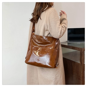 Dettaglio di una grande borsa in pelle lucida marrone indossata con un cappotto di lana beige