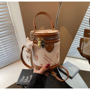 Detail of a beige cylinder bucket bag featuring brown leather trim and a cute bear charm