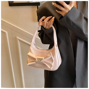 Close-up of pink crescent handbag featuring a large bow and metallic triangle logo detail