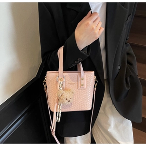 Close-up of pink woven bucket bag featuring plush bear charm and silk scarf detail