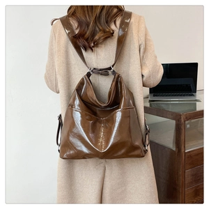 Borsa a secchiello marrone scuro lucido indossata come zaino su cappotto beige