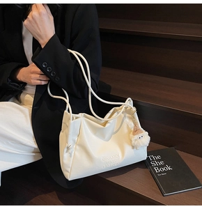 Detail of white leather tote bag with MIKAXIQI logo and plush monster charm decoration