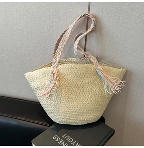 Dettaglio borsa da spiaggia in paglia beige con manico intrecciato pastello e frange