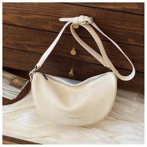 Detailed close-up of a cream moon-shaped crossbody bag with silver zipper and brand logo