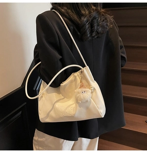 Detail of cream tote bag featuring embossed logo and a white plush monster charm