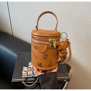 Close-up of textured brown leather cylinder bag with bear prints and a matching charm