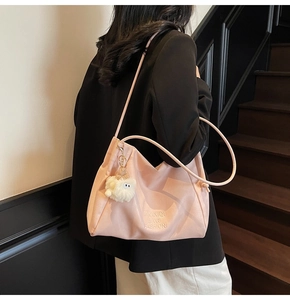 Pink tote bag with embossed letters and white plush charm on model in casual setting