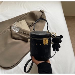 Detail of black cylinder bag featuring teddy bear charms and golden hardware