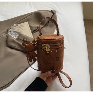 Detail of a brown textured barrel bag with Keddy Bear University logo and bear charm
