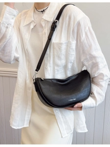 Modern black leather crescent shoulder bag with silver hardware on a female model