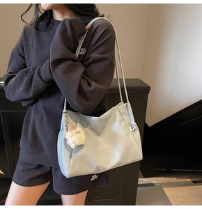 Detail of light blue tote bag with plush pendant and knotted side on a female model