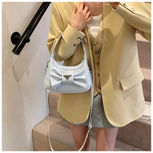 Detail view of white handbag with large bow, metal triangle logo and yellow blazer contrast