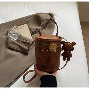 Detail of a brown leather cylinder bag with teddy bear print and matching bear charm