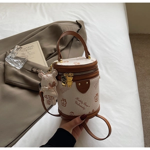 Detail view of a vintage beige cylinder bag with teddy bear university print and charm