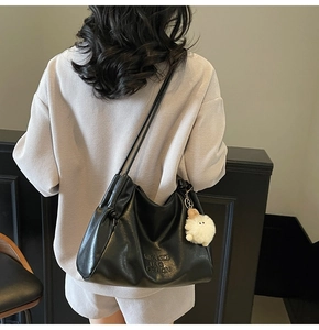 Detail of a black faux leather tote bag with a small white monster plush charm accessory