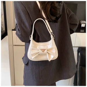Close-up of a creamy white bow shoulder bag with a gold triangular metal accent on a model