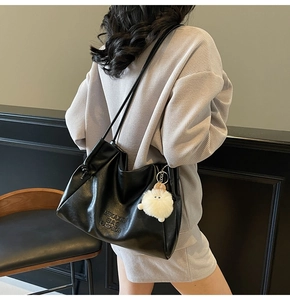 Detail of black leather tote bag with MIKA XQI embossing and white fluffy keychain